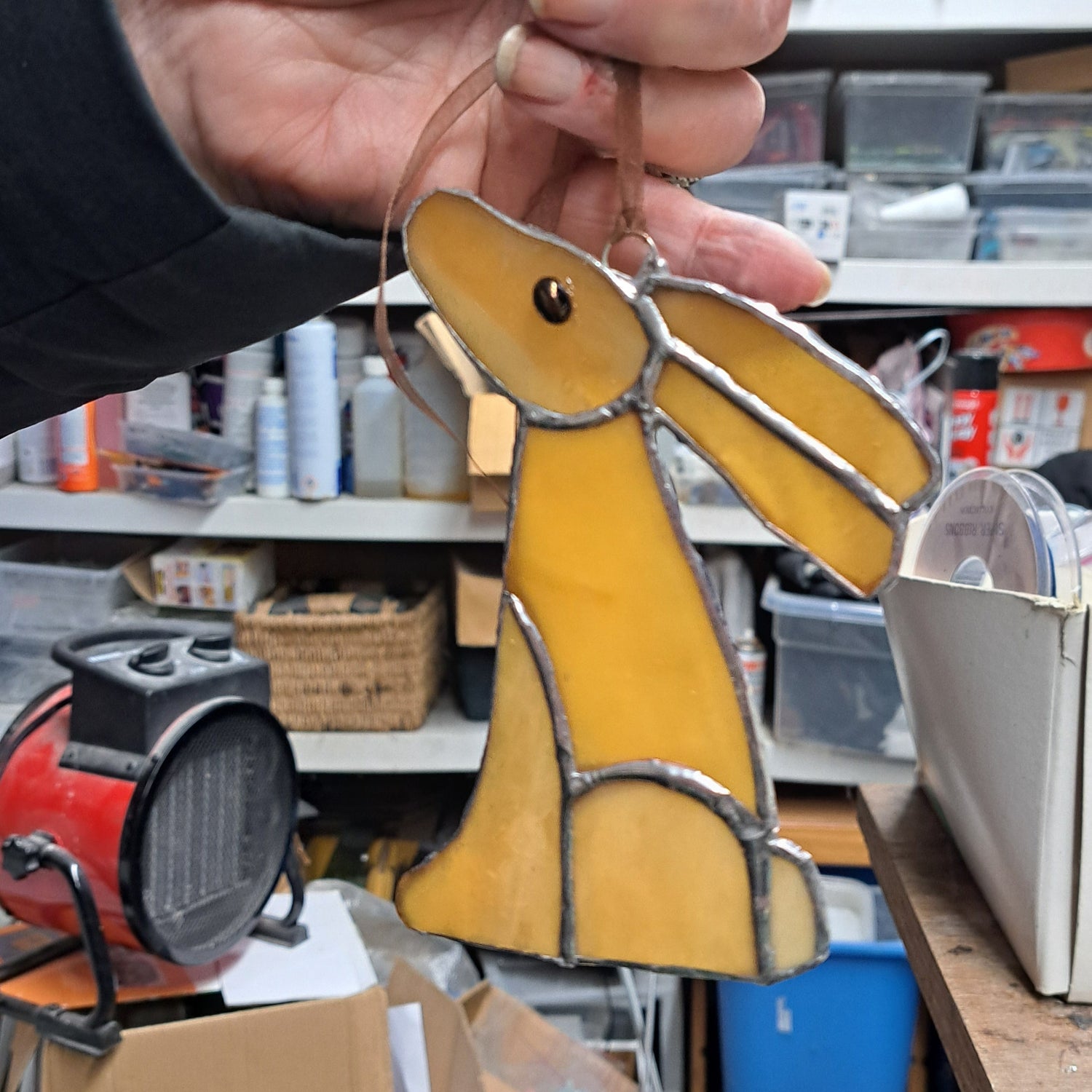 Hand holding a yellow glass rabbit ornament in a workshop.