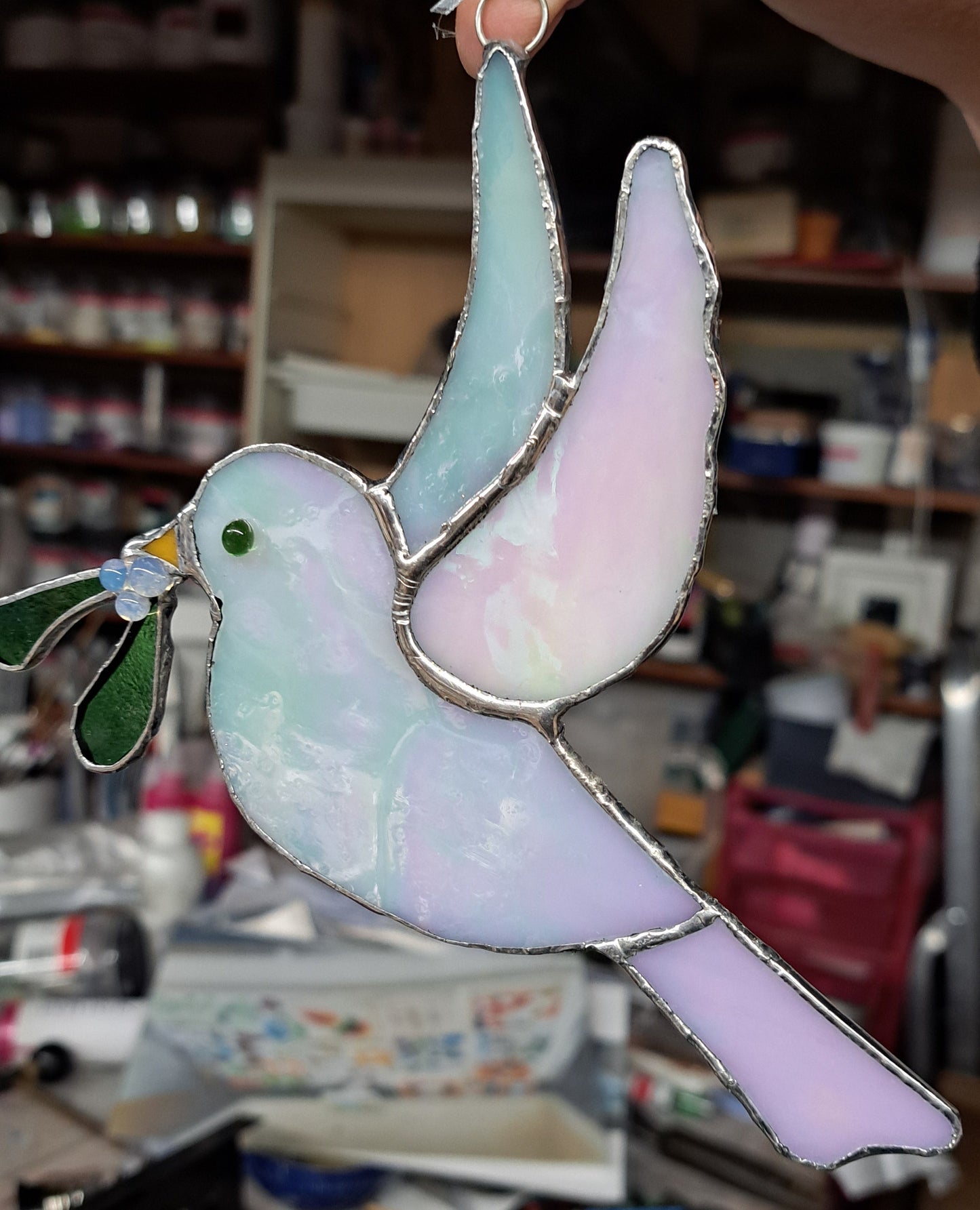 Stained glass dove held by a hand in a workshop setting